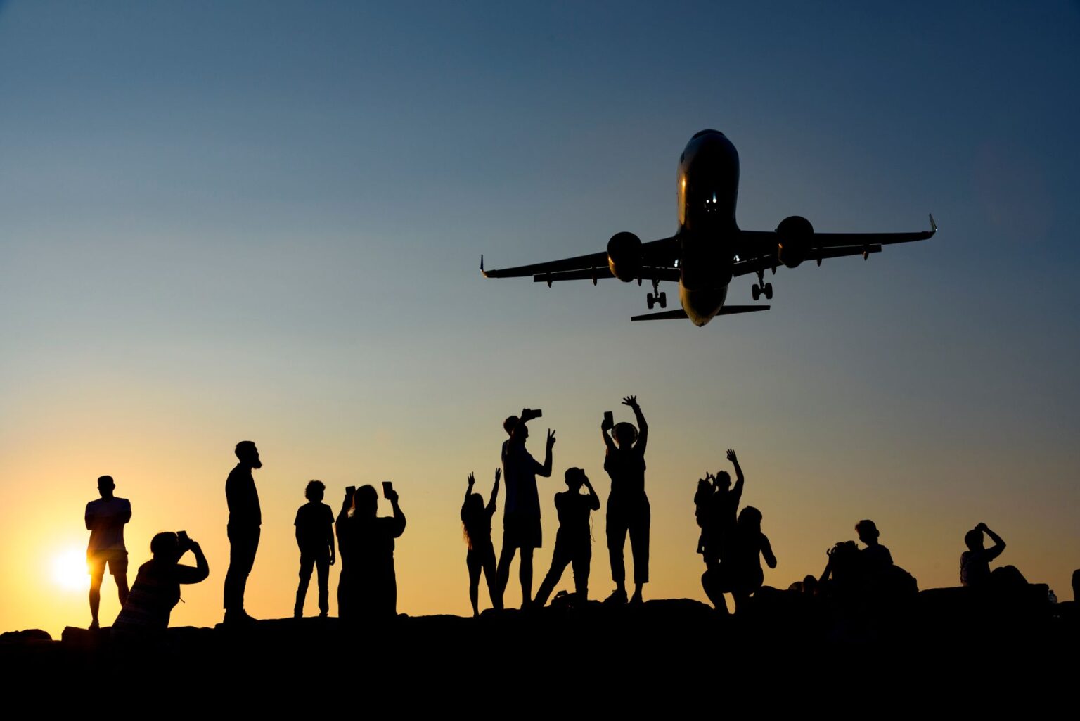 IATA summer travel forecast 2026 — A dynamic silhouette of people photographing an airplane during a vibrant sunset.